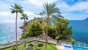 A pool area with a view of the sea, surrounded by palm trees and a rocky island. - Panorama by Interhome (Altea)