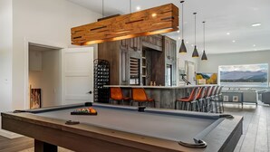 Une table de billard dans un salon moderne, avec un plafond en bois et des sièges de bar.