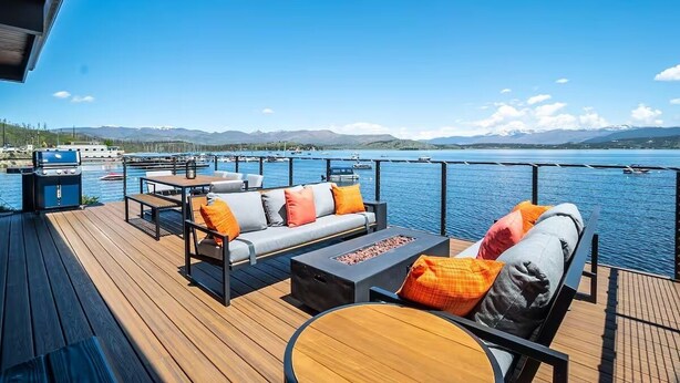 Une terrasse avec coin salon extérieur, un barbecue et une vue sur un lac et des montagnes.