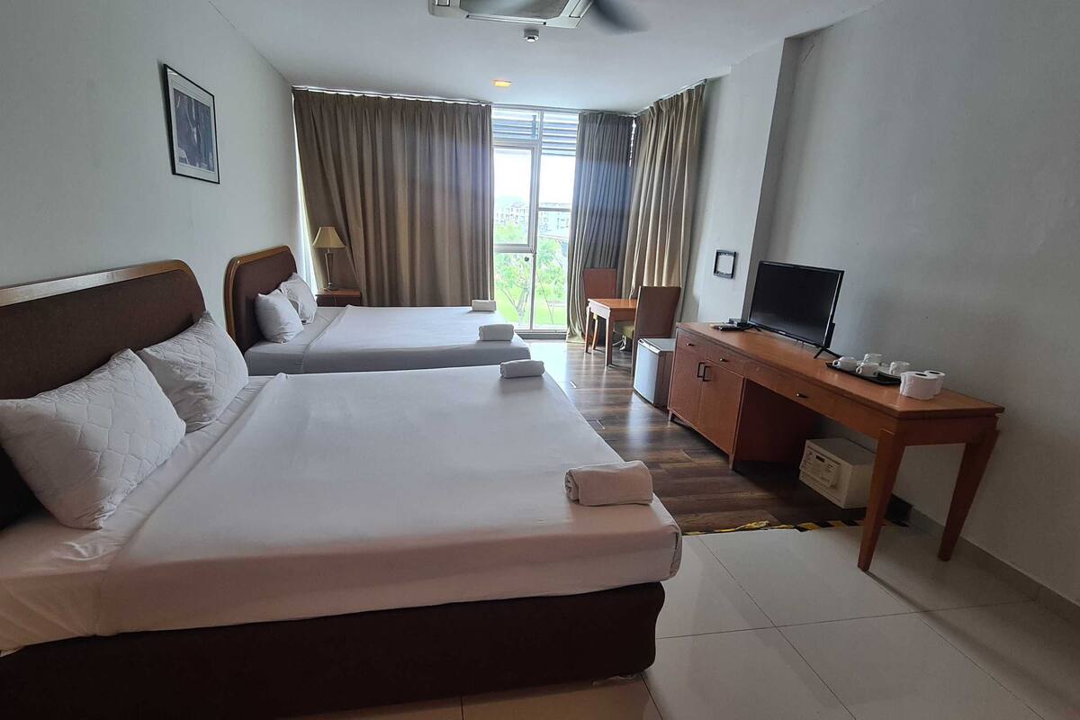 A hotel room with two beds, a desk with a television, and a view of the outdoors.