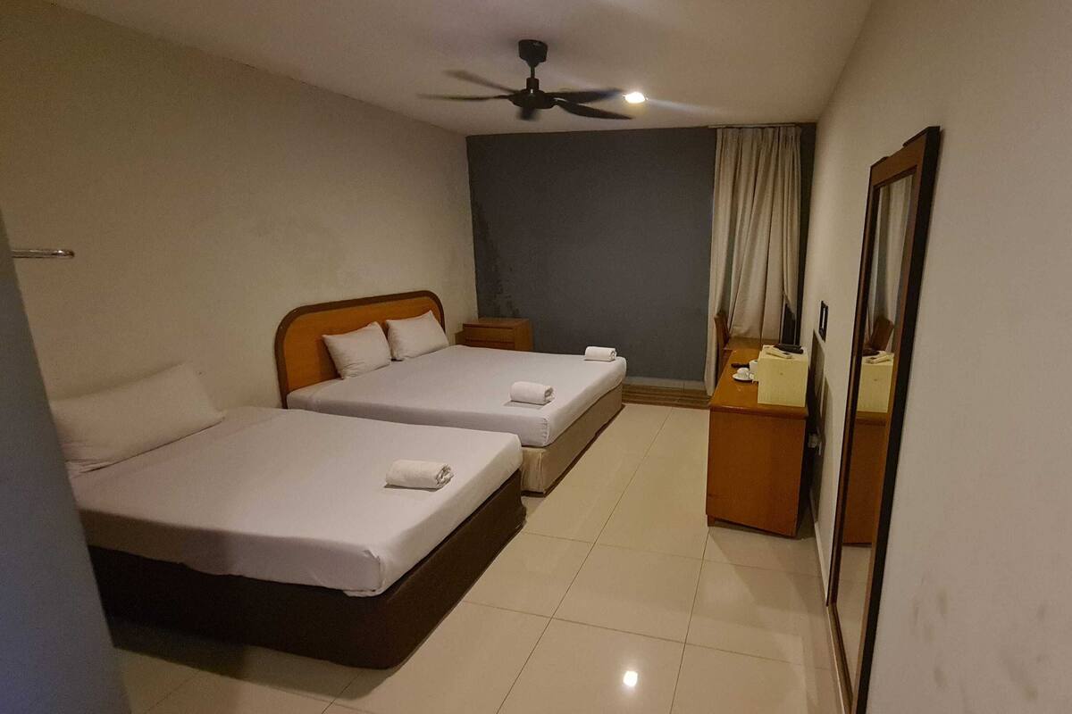 A hotel room with two beds, a desk, a chair, a ceiling fan, and a mirror.