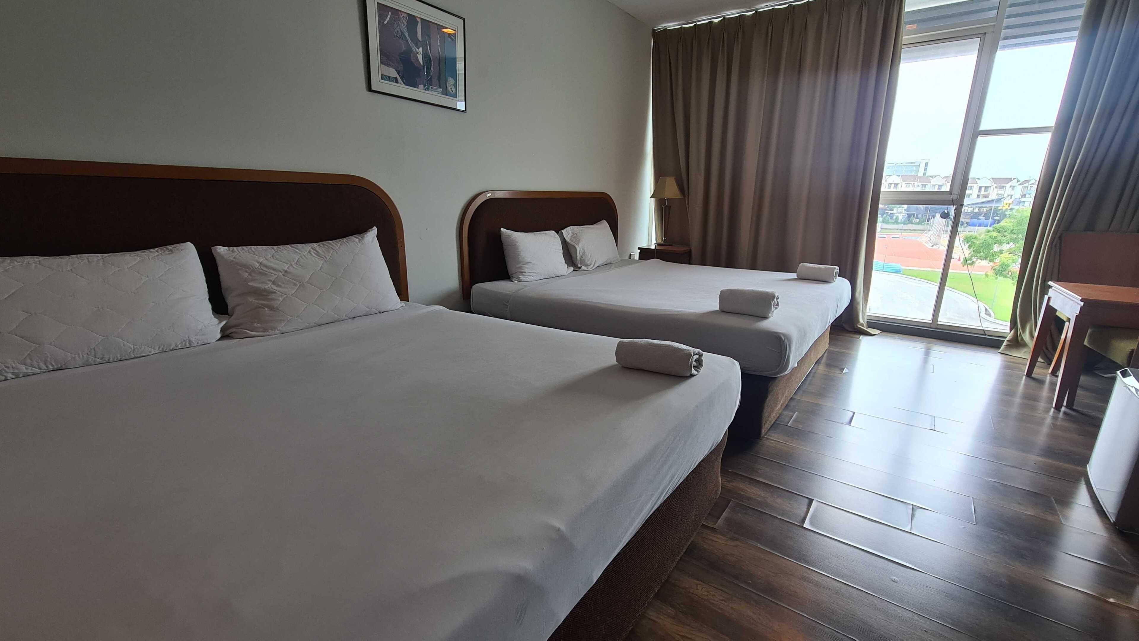 A hotel room with two beds, a large window with curtains, a wooden floor, and a framed picture on the wall.