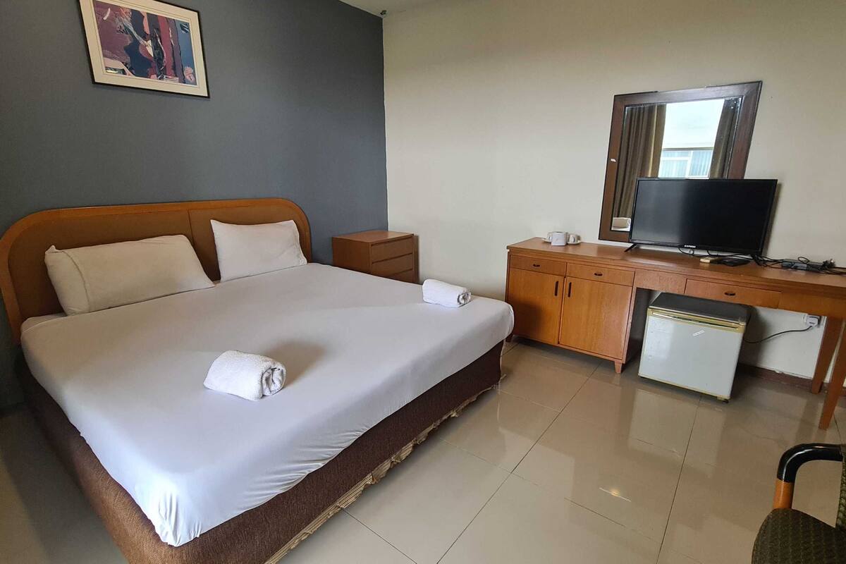 A hotel room with a bed, a desk with a television, a small refrigerator, and a chair.