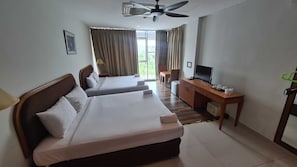 Ein Hotelzimmer mit zwei Betten, einem Schreibtisch mit Fernseher und einem Deckenventilator.