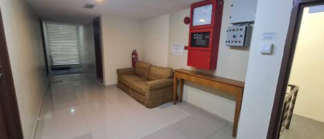 A hallway with a fire extinguisher, a red emergency control panel, and a wooden table.