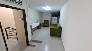 A hallway with a reception desk, a green sofa, and a chair. There is a sign above the door and a security camera on the wall. - Hotel O De Melor Bangi Gateway (Bandar Baru Bangi)