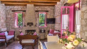 Una habitación acogedora con paredes de piedra, chimenea, ventanas con marcos rosados y techo de madera.