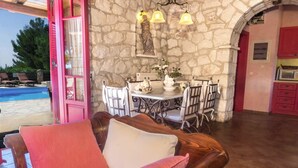 Un espacio de estar acogedor con pared de piedra, una mesa de comedor preparada para cuatro personas y una piscina visible a través de una puerta rosa.