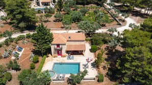 Una casa de dos pisos con piscina, rodeada de árboles y un jardín.