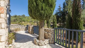 A stone pathway leading to a stone wall with a metal gate, surrounded by greenery and trees. - Villa Nephos - Beautiful sea views (Koiliomenos)