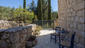 A stone patio with a table and chairs, surrounded by stone walls and tall trees. - Villa Nephos - Beautiful sea views (Koiliomenos)