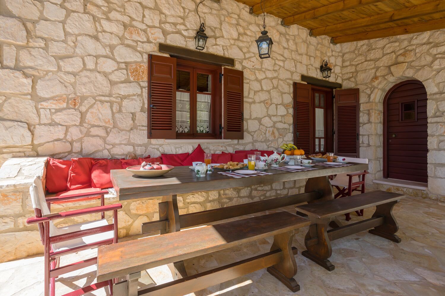 A stone-walled outdoor dining area with wooden benches and a table set for breakfast.