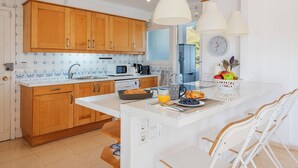 A modern kitchen with wooden cabinets, a white countertop, and a breakfast setup including fruits and pastries.