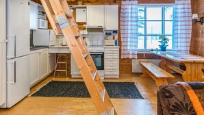 Een kleine keuken met witte kastjes, een magnetron en een kookplaat. Een houten trap staat tegen de muur en er is een raam met gestreepte gordijnen.