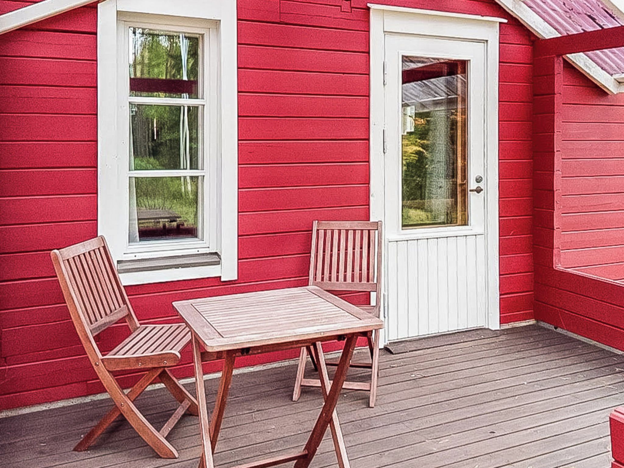 A red wooden building with a porch, two wooden chairs, and a table.