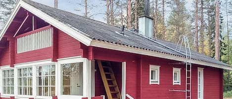 Una cabaña roja de madera con chimenea, una escalera y una ventana con marco blanco.