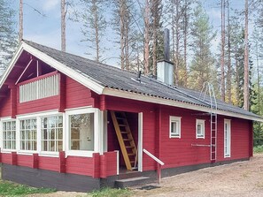 Una cabaña roja de madera con chimenea, una escalera y una ventana con marco blanco.