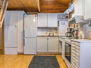 Kompakti keittiö, jossa on valkoiset kaapit, jääkaappi, mikroaaltouuni, kahvinkeitin ja liesi.