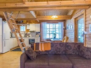 Un interior acogedor de cabaña con detalles de madera, un sofá, una mesa de comedor y una zona de cocina.