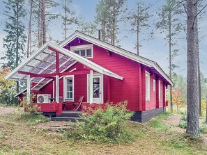 Une cabane rouge avec un toit en pente, un porche à l’avant et des panneaux solaires.