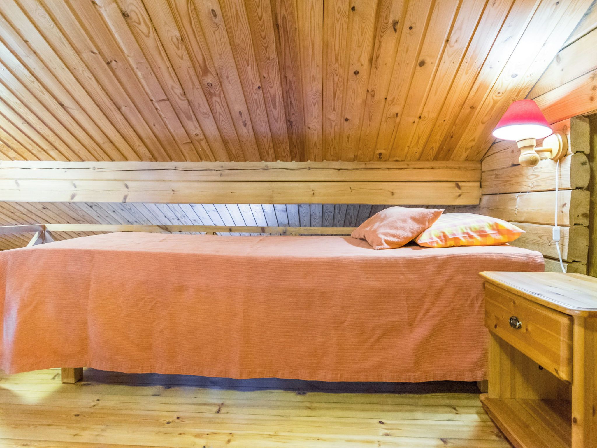 Una habitación de cabaña de madera con una cama, una mesita de noche y una lámpara fijada a la pared.