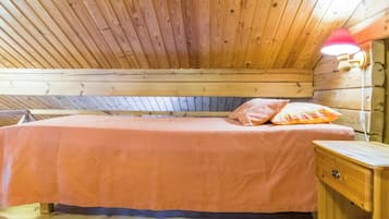 Una habitación de cabaña de madera con una cama, una mesita de noche y una lámpara fijada a la pared.