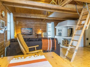 L’intérieur d’un chalet accueillant, avec un plafond en bois, un téléviseur, un canapé, un fauteuil et une échelle.