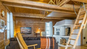 Een gezellig houten blokhut interieur met een houten plafond, een televisie, een open haard en een ladder.