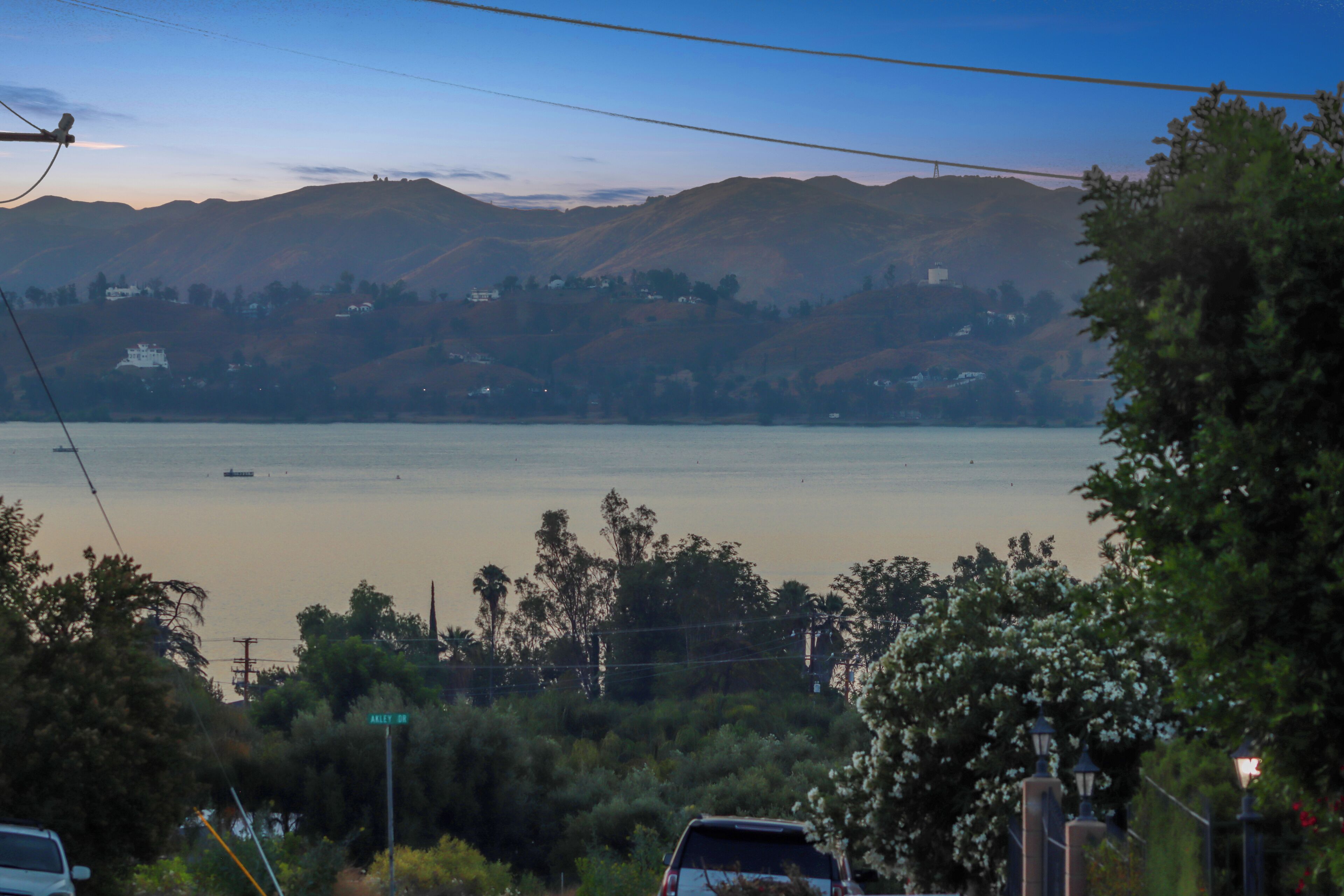 Vista de un lago con montañas al fondo, un coche aparcado en primer plano y una señal de calle a la vista.