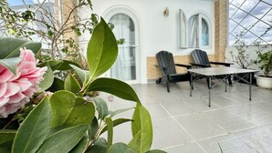 Ein überdachter Patio-Bereich mit Tisch und Stühlen, Topfpflanzen und Blick auf den Himmel durch eine Glasdecke.