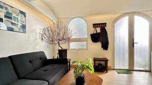 Ein modernes Wohnzimmer mit einer schwarzen Couch, einem Couchtisch aus Holz mit einer Pflanze, einem großen Fenster und einer Tür mit einer Schiebeglasplatte.
