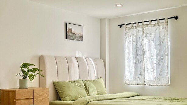 Ein Schlafzimmer mit zwei Betten, einer Zimmerpflanze, einem Nachttisch und einem Fenster mit Vorhang.