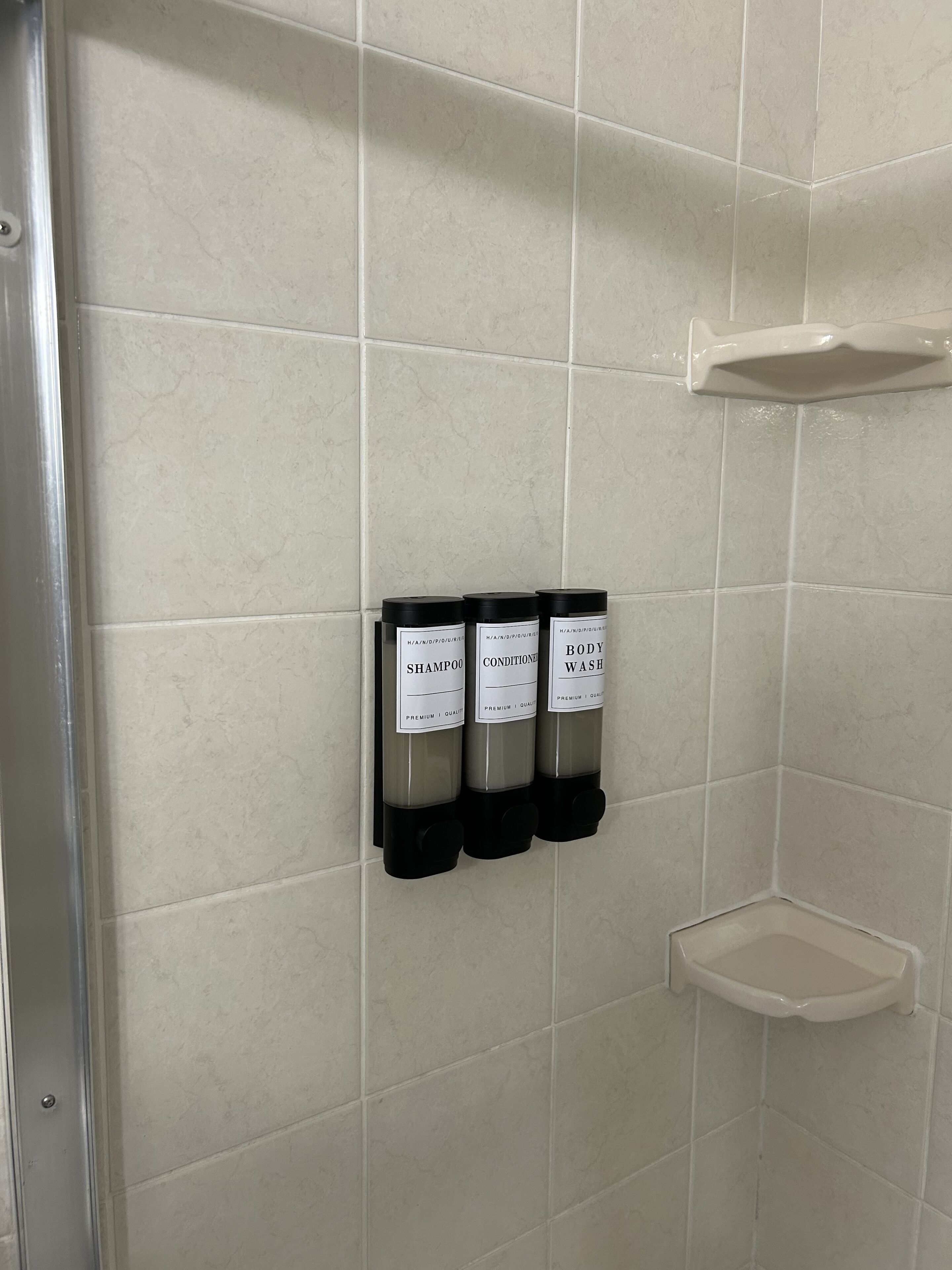 Une salle de bain équipée de trois distributeurs étiquetés « shampoing », « après-shampoing » et « gel douche ».