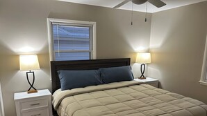 Un dormitorio con una cama, dos mesitas de noche, dos lámparas, una ventana con persianas y un ventilador de techo.