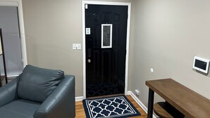 Una habitación con una puerta negra, un sofá gris, una mesa de madera y una alfombra estampada.