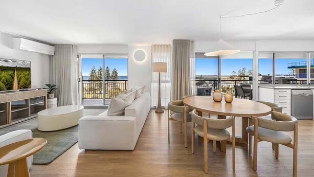 A modern hotel room with a living area, dining space, and a balcony with a view.