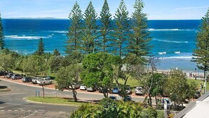A coastal view with a parking area, trees, and a beach in the background.