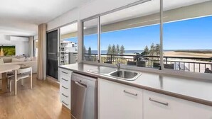 A modern kitchen with a large window, a dishwasher, and a dining area with a view of the sea.
