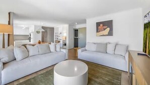 A modern living room with two white sofas, a round coffee table, and a painting on the wall.