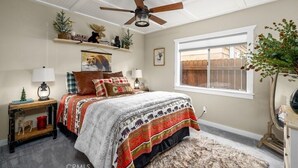 A bedroom with a bed, a ceiling fan, a window, and a nightstand with a lamp.