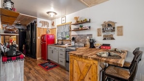 A rustic kitchen with wooden cabinets, a red refrigerator, and a wooden island with a coffee machine.