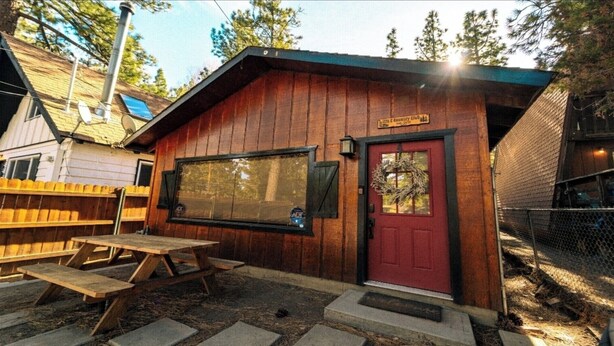 A rustic wooden cabin with a red door, a large window, and a picnic table outside.