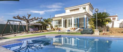 Ein Schwimmbecken mit Fliesenbordstein, umgeben von einer Rasenfläche und einem Haus mit Balkon.
