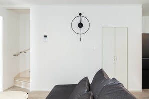 A modern living room with a sofa, a wall-mounted clock, a wardrobe, and a staircase.