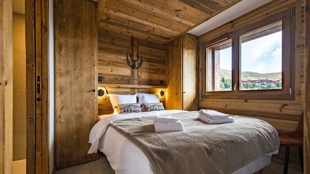 Une chambre dans une cabane en bois, avec un lit, une chaise et une fenêtre donnant sur un paysage agréable.