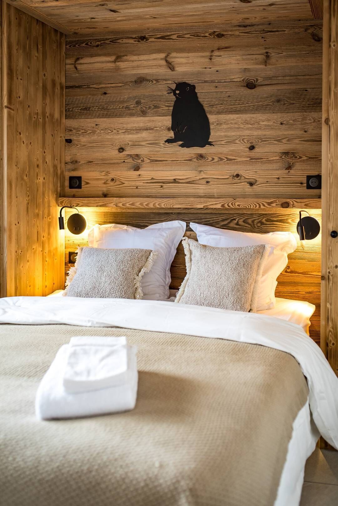 A cozy wooden cabin-style bedroom with a bed, pillows, and a blanket.