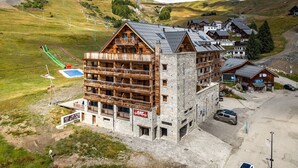 Un bâtiment en bois à plusieurs étages, doté de balcons, avec un télésiège à proximité et un paysage montagneux en arrière-plan.