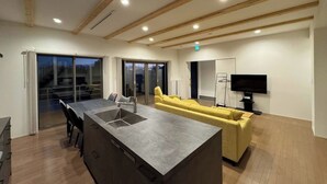 Eine moderne Küche mit einer zentralen Kochinsel, einem gelben Sofa, einem Flachbildfernseher und einer Glastür, die zu einem Außenbereich führt.