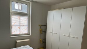 A bedroom with a bed, a wardrobe, a radiator, and a window with blinds. - Vacation apartment Lehesten Zinkenweg (Lehesten)