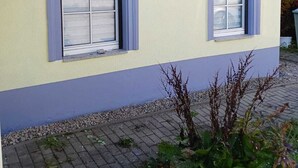 A two-story building with a yellow and blue exterior, two windows with shutters, and a visible gutter system. - Vacation apartment Lehesten Zinkenweg (Lehesten)